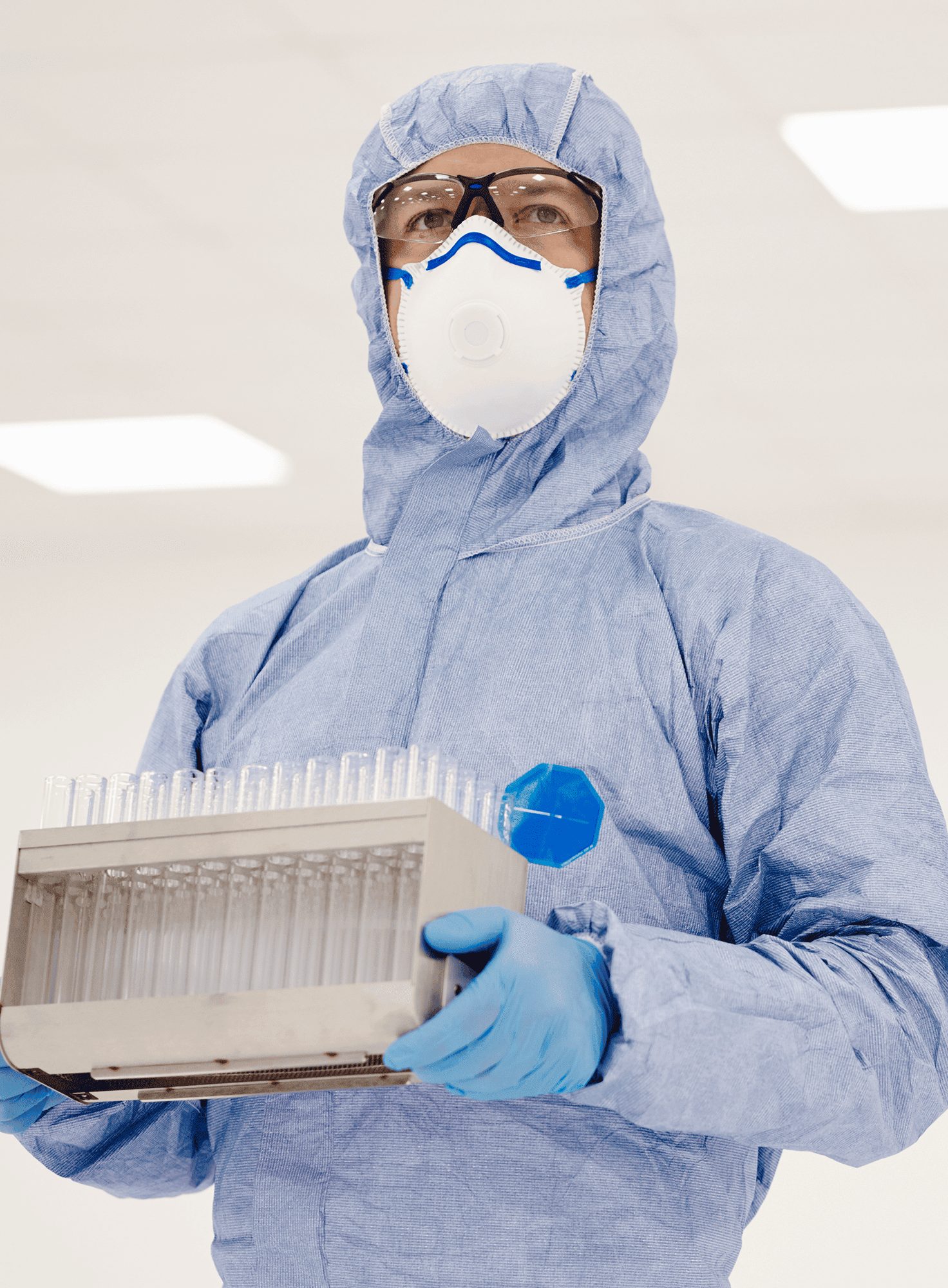 Ein SKAN-Mitarbeiter in einem hellblauen Schutzanzug und in der Hand ein Set Reagenzgläser.